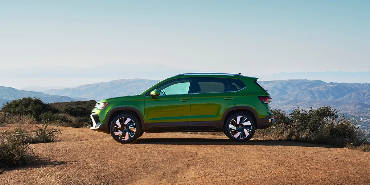 Side profile of Volkswagen Taos SUV in bright green, parked on a mountain overlook with panoramic landscape views.