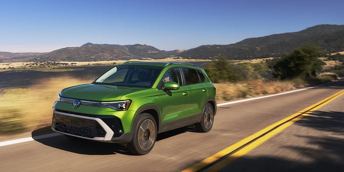 Volkswagen Taos SUV driving through a winding road at sunset, emphasizing its sleek rear profile and signature LED taillights.